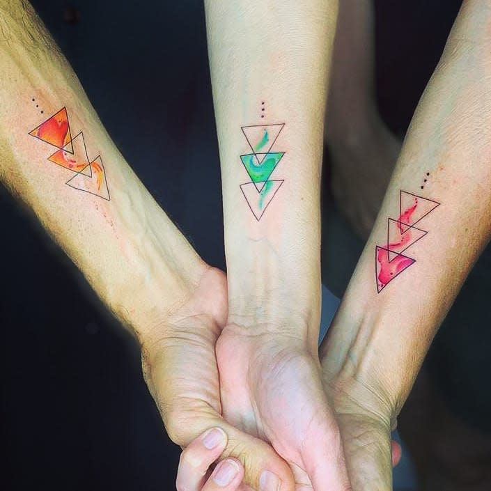 Three arms with matching geometric triangle tattoos in orange, green, and red colors